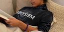 Person wearing EESystem Hoodie, reading a book on a couch.
