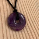 EEMedallion Amethyst on a black cord against a beige woven background