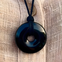 EEMedallion Black Obsidian on a textured beige fabric background