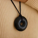 EEMedallion Hawk Eye on a black cord against a beige fabric background.