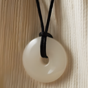 EEMedallion White Jade on a black cord against a light wood background

