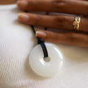 EEMedallion White Jade on a black cord with a hand wearing a gold ring in the background.