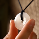 EEMedallion White Jade on a black cord held between fingers against a blurred background