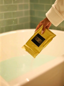 Hand holding EESalt in front of a bathtub.