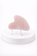 Pink Gua Sha Rose Quartz tool on a white stand